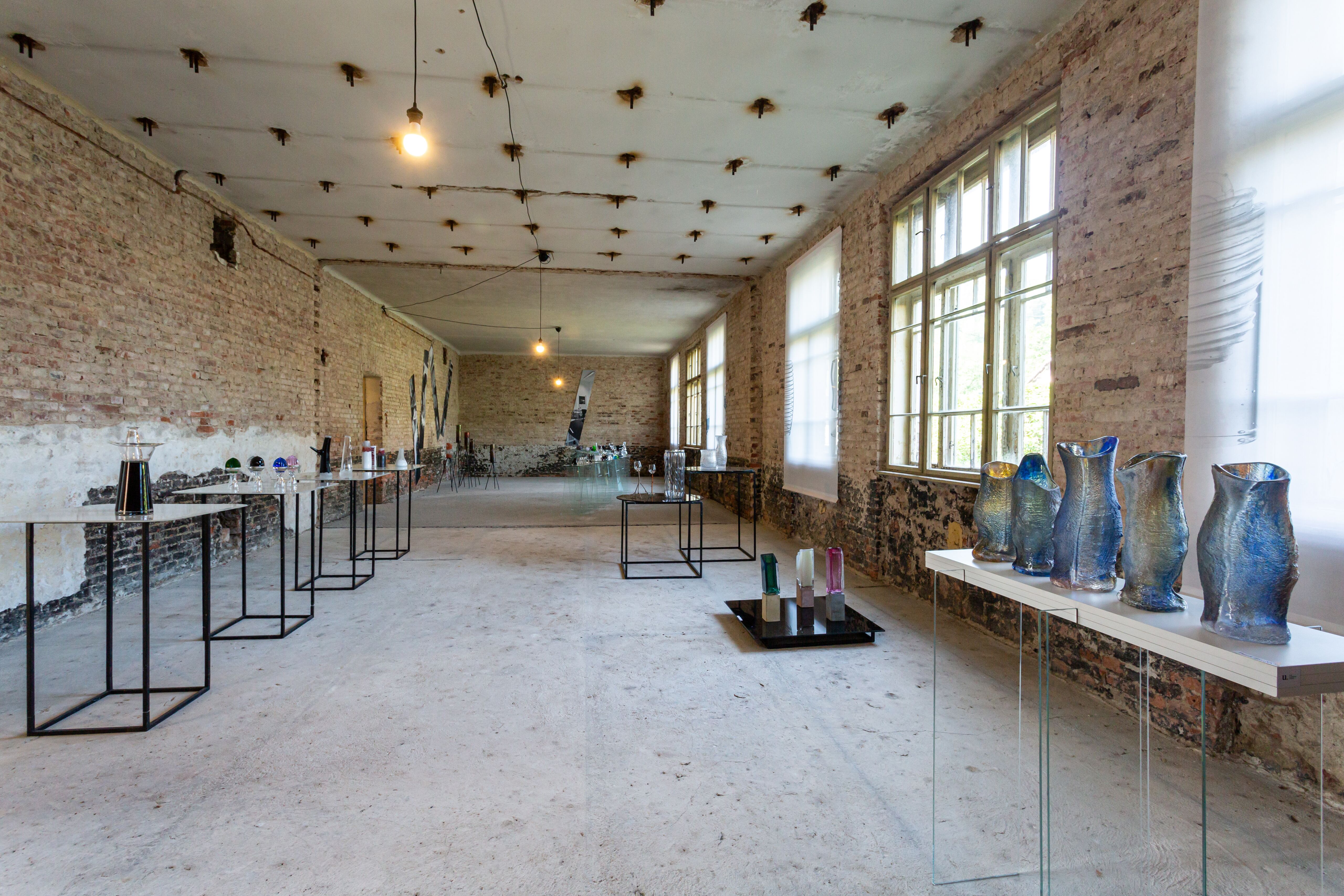 Celkový pohľad na miestnosť industriálneho interiéru, v ktorom je nainštalovaná výstava skla. 