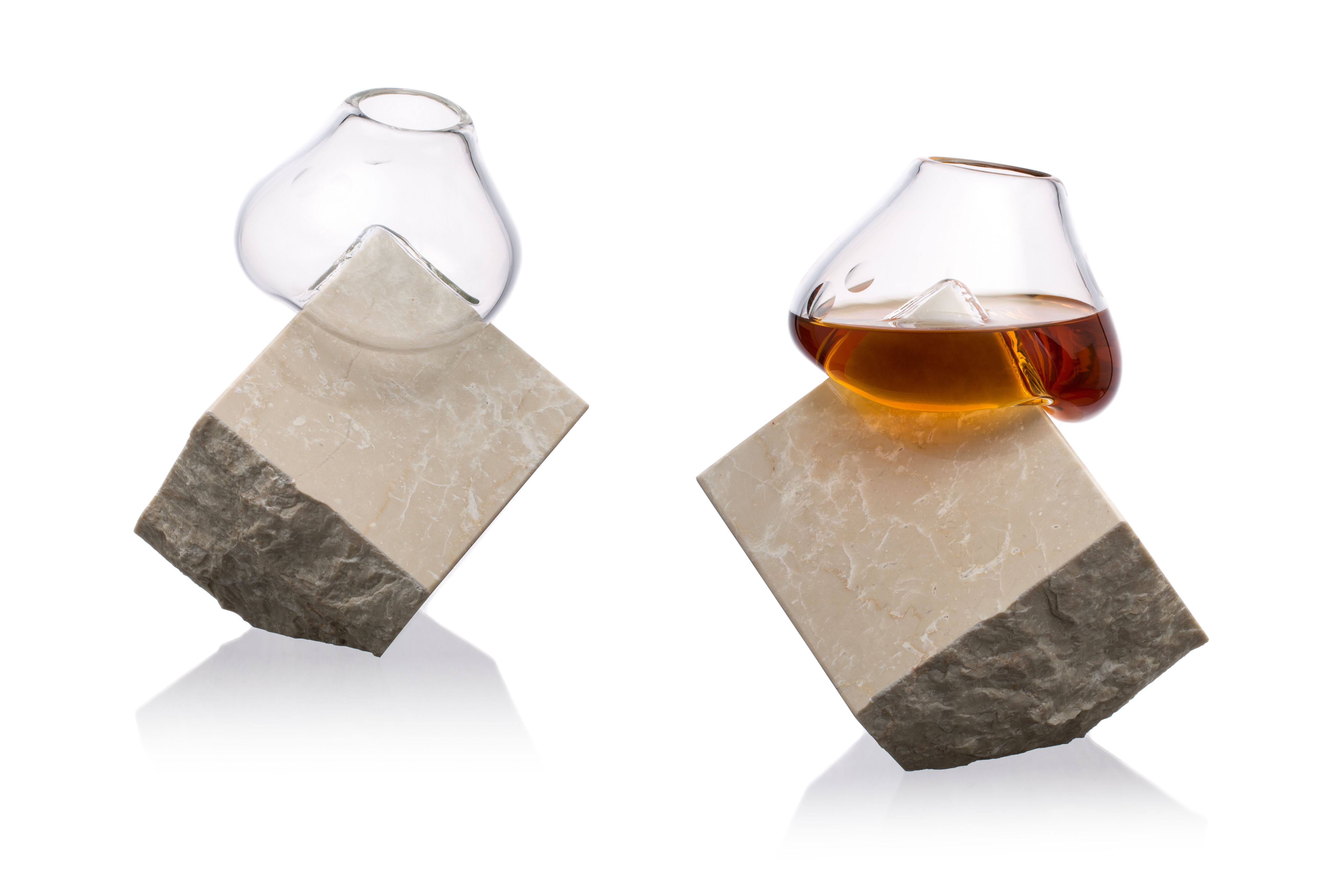 Dva netypické číre poháre zo skla určené na koňak vsadené do kociek z kameňa na bielom pozadí. 
